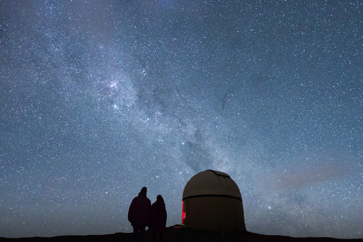 Couple next to observatory dome with milky way above
